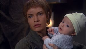 T'Pol is looking at someone off-screen. She looks dirty and tired, and she is holding a small baby in her arms.