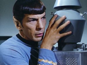 Spock is mind-melding with a faceless robot. His fingers are splayed across its head, and he is looking at someone off screen.