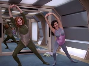Beverly and Deanna are in a gym on the Enterprise standing in front of a mirrored wall. They are doing stretching exercises, dressed in the most horrendous sparkly leotards imaginable.