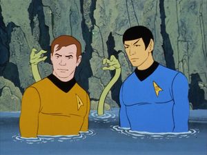 A frame from a cartoon. Spock and Kirk are standing in front of a cliff, chest deep in water. Behind Kirk, two sinuous green arms emerge from the water to menace him.