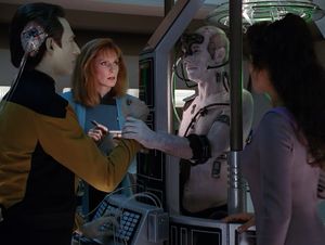 In the laboratory, Beverly and Deanna look on as Picard, still covered in Borg implants, reaches out a human hand to grab Data's forearm. The two men look directly at each other.