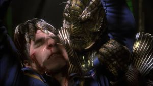 In the brig of a Xindi starship, Archer is hanging by his arms from the  ceiling. He has been beaten, and there is blood on his face and in his mouth. Behind him, holding him by the head, is the menacing figure of a Xindi-Reptilian. 