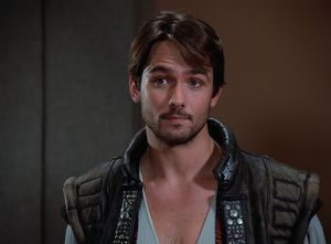 It's beautiful Billy Campbell as Thadiun Okona, looking so innocent. He's got a scruffy beard, long hair, dark eyes and a little tuft of chest hair poking out of his pirate shirt.