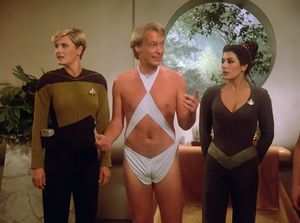 One of the Edo, a scantily-clad man with an exposed belly-button and a completely tucked dick, is standing between Yar and Troi. Yar appears to  be looking off camera at her agent, wordlessly pleading with him to get her out of this stupid show. Troi is looking disdainfully at him.