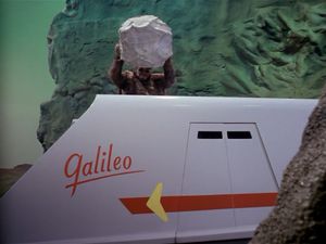 We're on an alien planet a green sky and rocky outcrops made of chicken wire and papier-mâché. The shuttlecraft Galileo, has landed here. Behind it, but towering over it, is a large apelike creater. He is holding a polystyrene rock above his head, about to bring it down on the roof of the shuttlecraft.