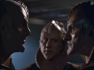 We see three Vaadwaur — ridiculous Voyager aliens who are supposed to look like cobras but who instead look like embarrassed white American actors each covered in five kilos of latex. Two of them look angrily at each other in profile. The one in the background looks uncertain.