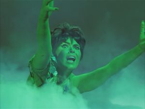 On the misty surface of a particularly unconvincing alien planet, a scantily-clad green-skinned Orion woman stretches out her hands. She looks terrified.
