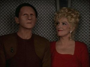 Odo and Lwaxana are standing in a turbolift. Odo is looking up at the ceiling, Lwaxana is smiling gently at him.