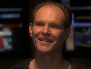 A close-up of the smiling face of Michael Eddington, who is apparently standing on the bridge of the Defiant.