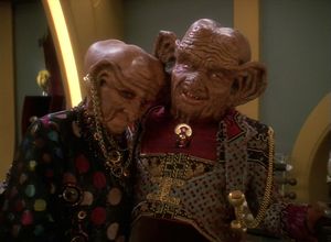 It's an elderly Ferengi couple: on the left is Moogie, a lady in a  polka-dotted dress and lots of gold jewellery. On the right is Grand Nagus Zek, a very wrinkled old man with huge hairy ears in an equally elaborate outfit. They both look terribly happy.