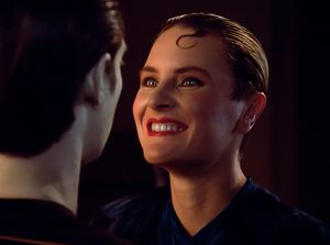 Tasha is heavily made up, with her hair slicked back and a kiss curl on her forehead. She is looking directly into Data's eyes as smiling toothily, as if she's just heard that Data is programmed in multiple techniques, a broad variety of pleasuring.