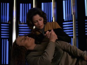 On the transporter pad, Klingon B'Elanna is lying with her head in human B'Elanna's lap, about to die from a phaser wound. They are holding hands.