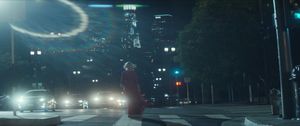 Agnes Jurati, in a flowing red dress, walks away from us across a city street at night as headlights and skyscrapers glow ahead of her.