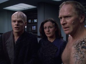 In sickbay, three ex-Borg drones stand in a line, looking pleadingly at someone off camera — a bald alien man, a beautiful Bajoran woman and an older man. All of them are scarred, and the older man is shirtless, with Borg implants emerging through the skin of his chest.