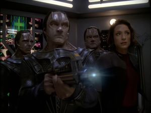 We're on the bridge of a Jem'Hadar spaceship. Three Cardassians — Damar, Garak and Rusot are here, along with Colonel Kira in a Starfleet uniform. Garak has just started to fire his gun at someone offscreen.