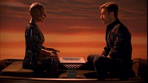 It's sunset. Two people are sitting in a dinghy facing one another. On the left, and orange lizard lady in a shiny jumpsuit: on the right is Trip in his Starfleet uniform. There is a bowl of white crystals between them.