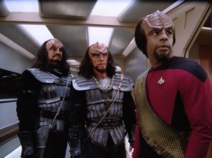 We're in an Enterprise corridor. There are three Klingons here. The two on the left are in traditional Klingon armor, but on the right is Worf, with his short Season 1 hair, looking concerned at something off camera.