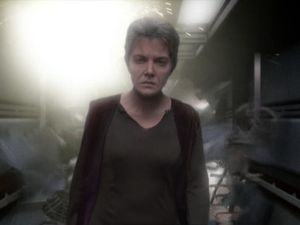 Older, grim and determined, Kes walks down one of Voyager's corridors, her jaw set, as the walls explode around her.