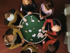 A shot from above — the bridge crew of the Enterprise-D are all sitting  around the poker table. Picard is dealing