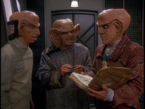 Quark, Rom and Grand Nagus Zek are standing in Quark's quarters. Quark has an elaborately bound book in his hand: he seems to be looking up from it in horror. Rom looks at him concerned. Behind them Zek is grinning happily, unaware of the consternation he is causing.